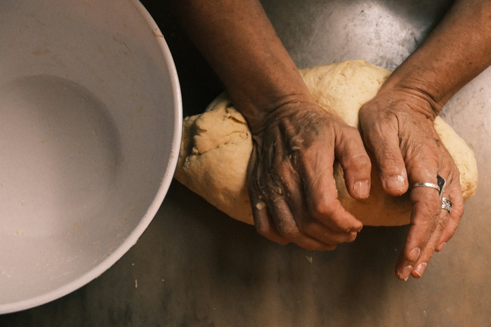 An older pair of hands kneading bread dough beside a mixing bowl