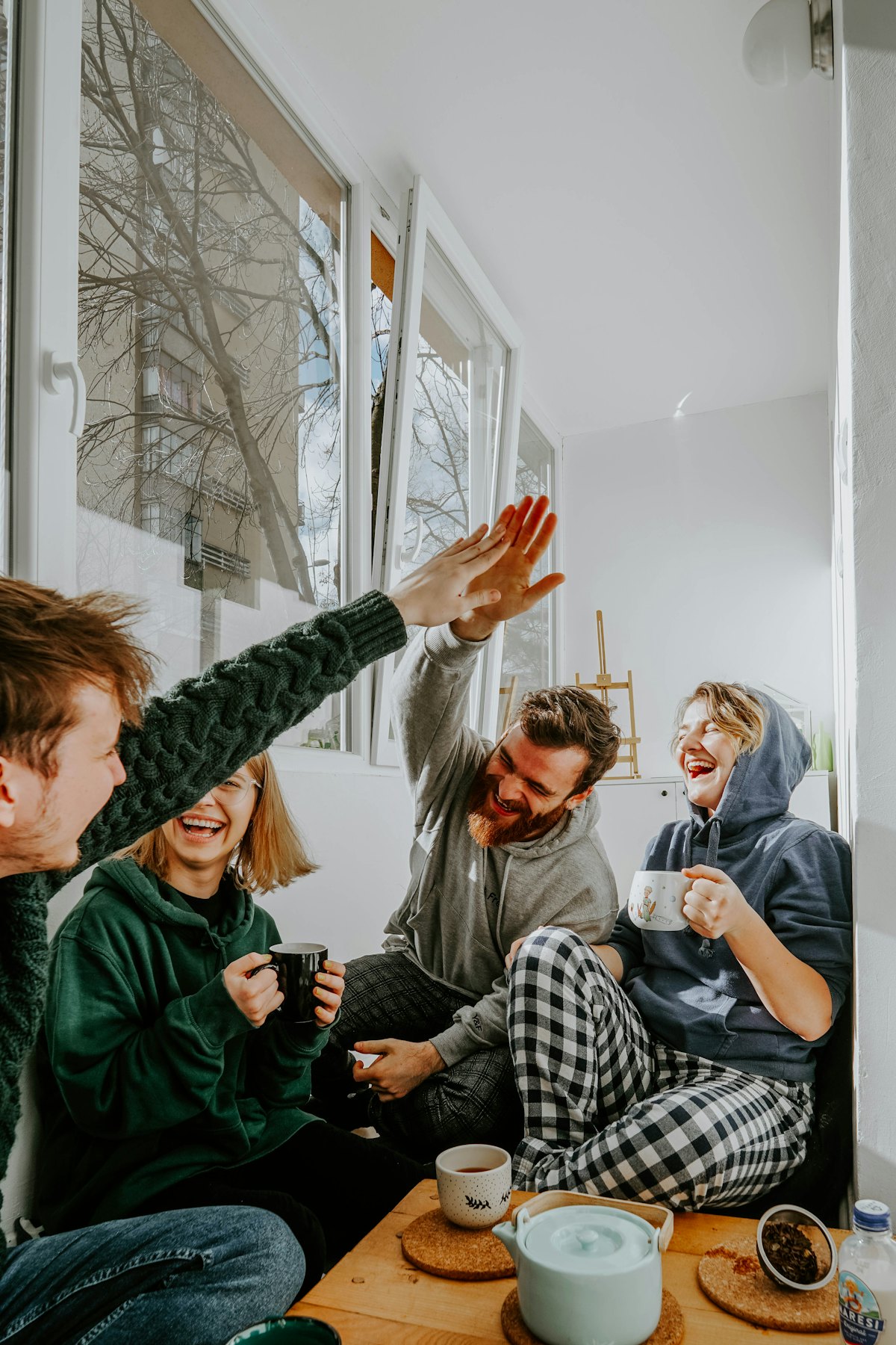 Four friends laughing over mugs of tea by a bright window