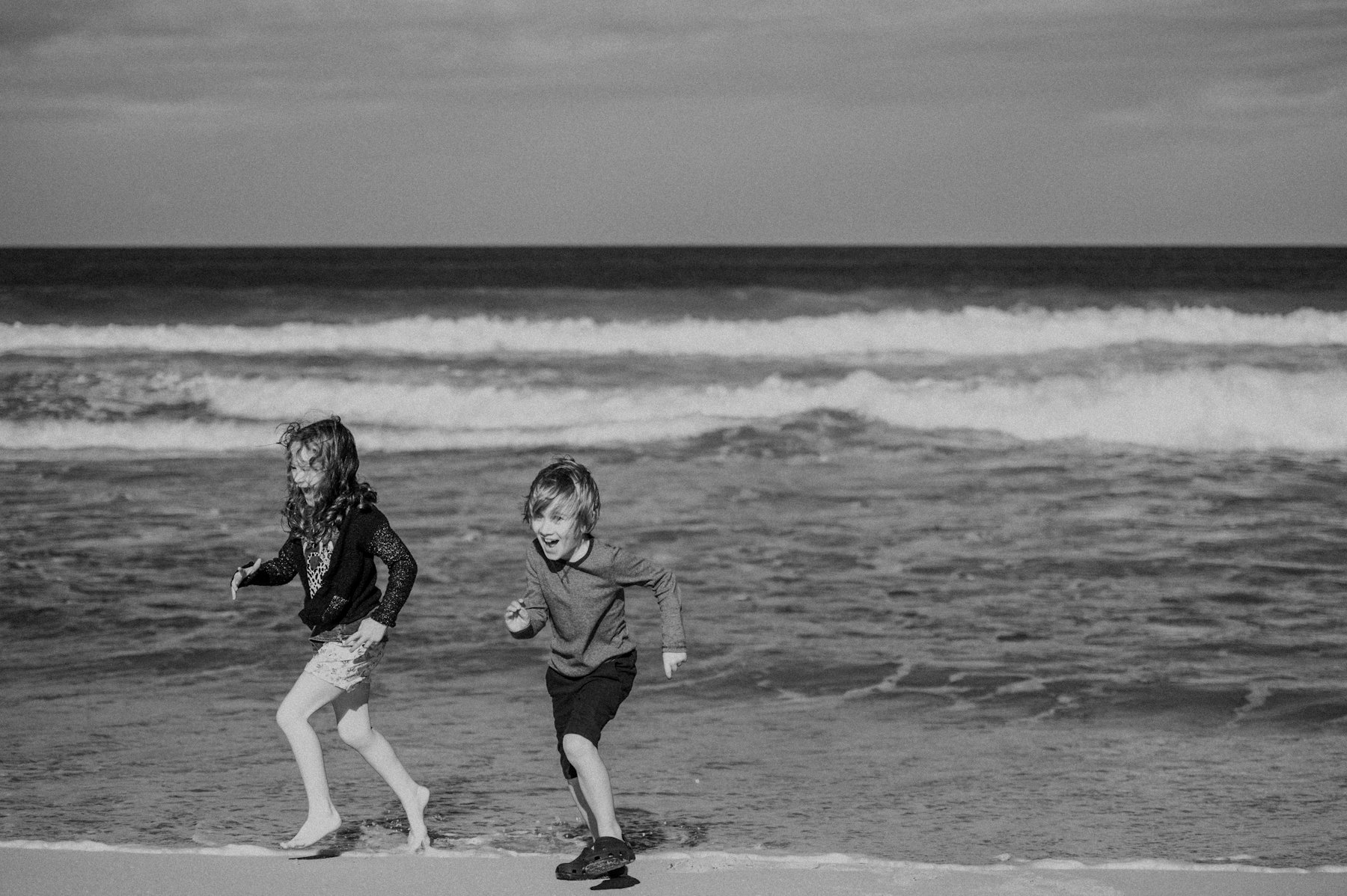 Two children running along the edge of the sea, in black and white